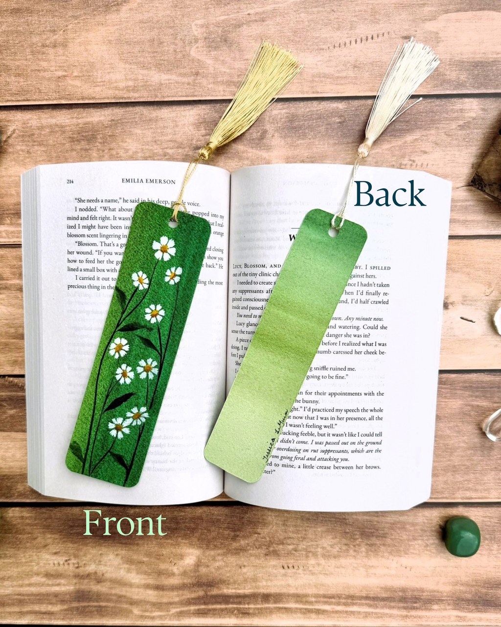 Two decorative bookmarks displayed on an open book on a wooden surface. One bookmark is a solid light green and reads 'Back', while the other is a green gradient with white chamomile floral patterns and a gold tassel, labeled 'Front'.